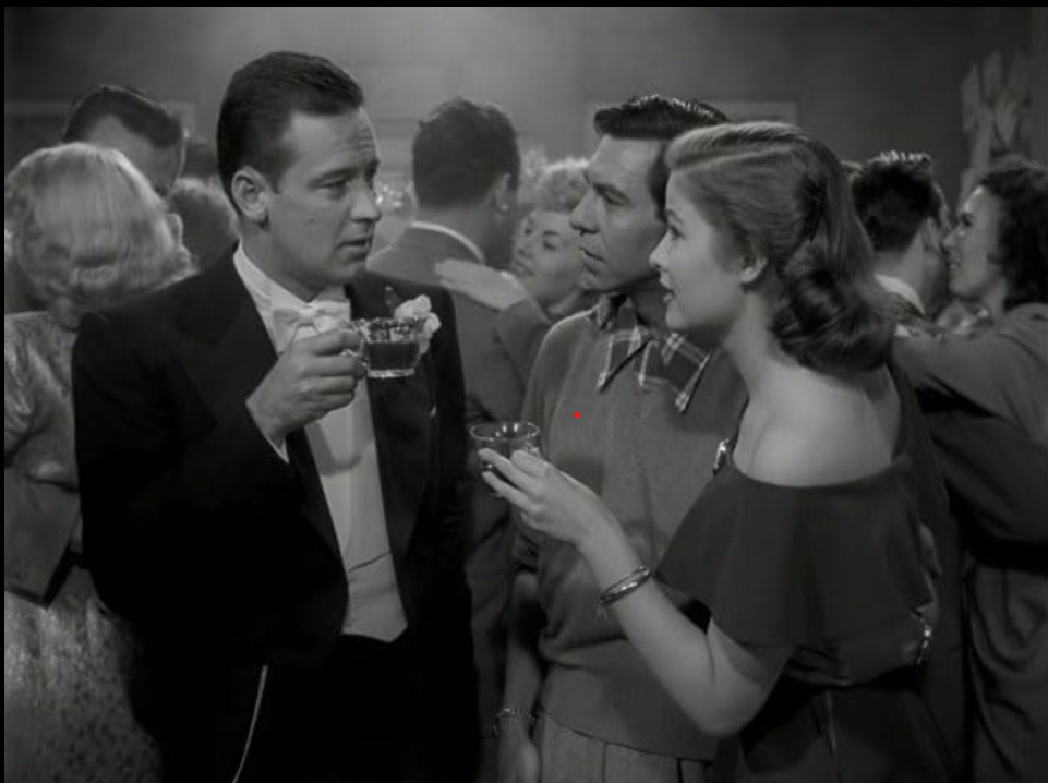 Man on left in dress suit is holding a cup while talking to a younger couple. The woman on the right is attractively dressed and the man in the middle looks plain.